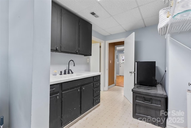 kitchen with dark cabinetry, light floors, visible vents, a sink, and a paneled ceiling