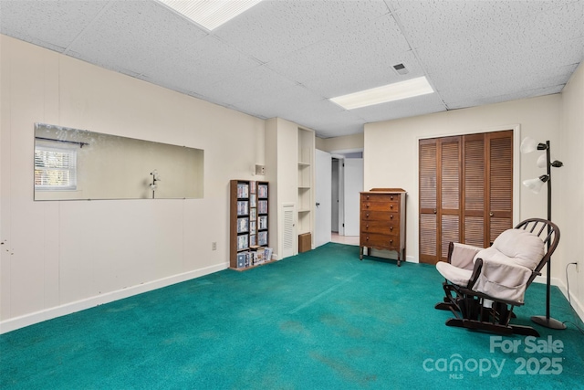 living area with a drop ceiling, baseboards, and carpet floors