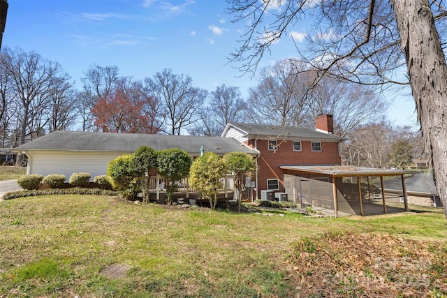 back of house featuring brick siding, a lawn, a chimney, a deck, and a sunroom