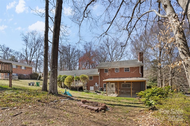 back of property with a yard, brick siding, a chimney, and a sunroom