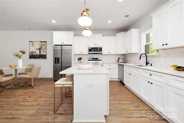 kitchen featuring a center island, decorative light fixtures, light countertops, appliances with stainless steel finishes, and a sink