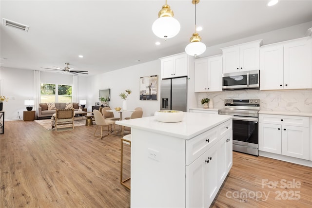 kitchen featuring decorative light fixtures, light countertops, appliances with stainless steel finishes, open floor plan, and white cabinetry