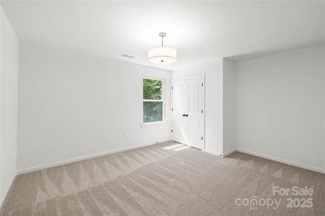 spare room featuring baseboards, visible vents, and light colored carpet