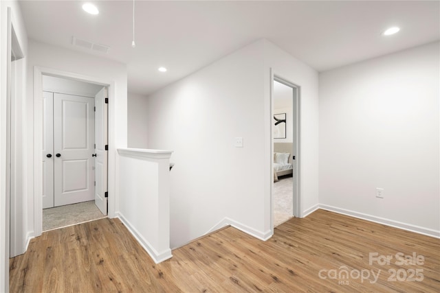 hall featuring visible vents, baseboards, an upstairs landing, light wood-style floors, and recessed lighting