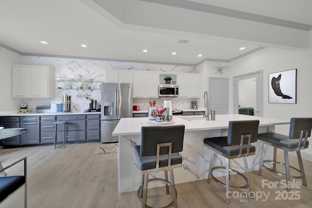 kitchen with appliances with stainless steel finishes, white cabinets, light countertops, and a center island with sink