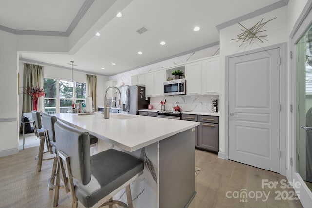 kitchen featuring visible vents, a kitchen breakfast bar, stainless steel appliances, crown molding, and light countertops