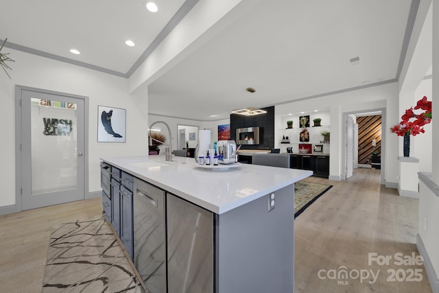 kitchen featuring a center island with sink, light countertops, open floor plan, a sink, and light wood-type flooring