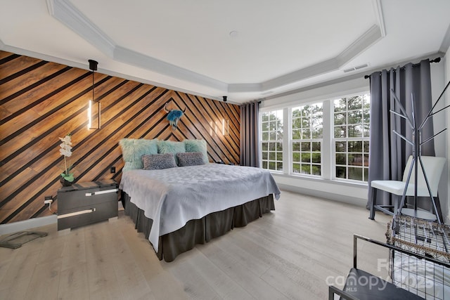 bedroom featuring ornamental molding, light wood-style flooring, a raised ceiling, and visible vents