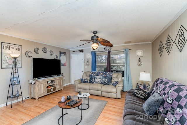 living area with a textured ceiling, a ceiling fan, light wood-style floors, baseboards, and crown molding