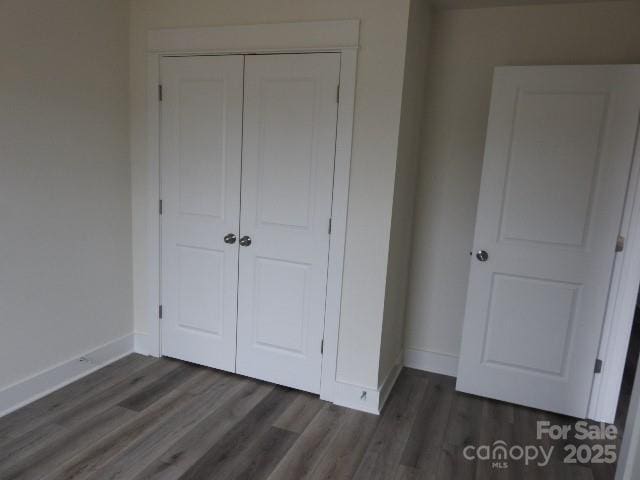 unfurnished bedroom featuring dark wood-style floors, baseboards, and a closet