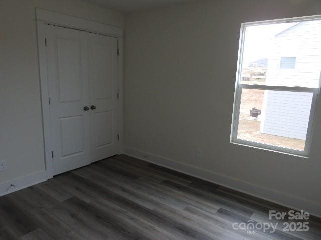 unfurnished bedroom featuring a closet, baseboards, and dark wood-type flooring