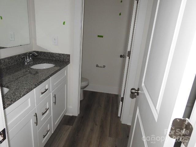 full bathroom with double vanity, toilet, a sink, wood finished floors, and baseboards