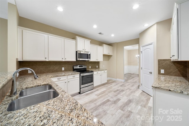 kitchen with stainless steel appliances, white cabinets, a sink, and light stone countertops