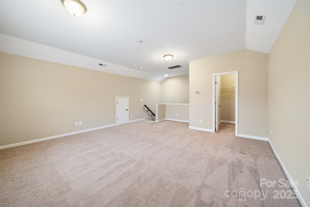 spare room featuring light colored carpet, lofted ceiling, visible vents, and baseboards