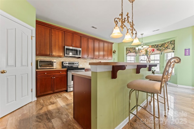 kitchen featuring pendant lighting, a toaster, stainless steel appliances, light countertops, and backsplash