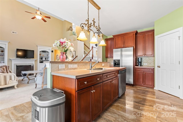 kitchen with stainless steel appliances, a center island with sink, light countertops, and a sink