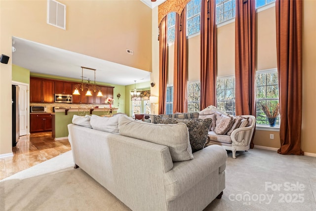 living room featuring a towering ceiling, an inviting chandelier, visible vents, and light colored carpet