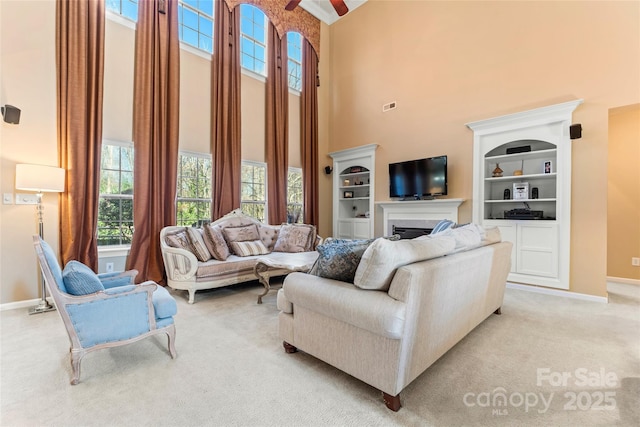 living room with light carpet, a fireplace, baseboards, and a high ceiling