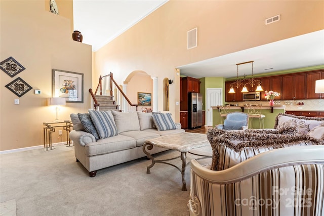 living room with light colored carpet, a towering ceiling, visible vents, stairway, and ornate columns