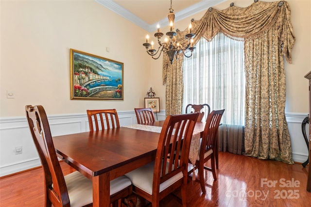 dining room with a wainscoted wall, ornamental molding, wood finished floors, a decorative wall, and a notable chandelier