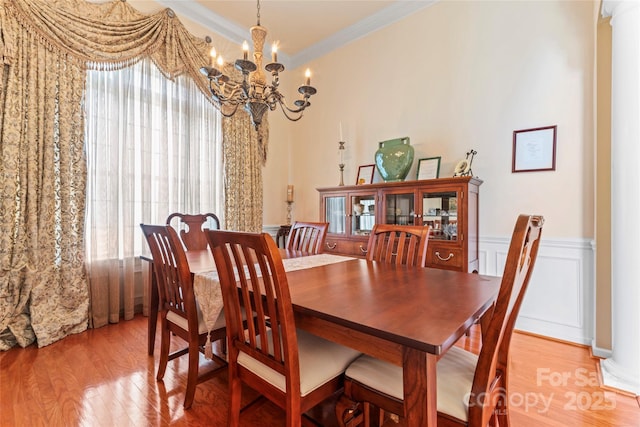 dining room with light wood-style floors, ornamental molding, a decorative wall, and a wainscoted wall