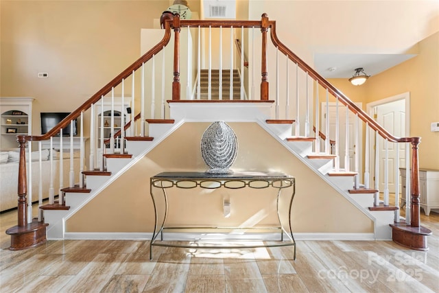 stairs with a high ceiling, visible vents, baseboards, and wood finished floors