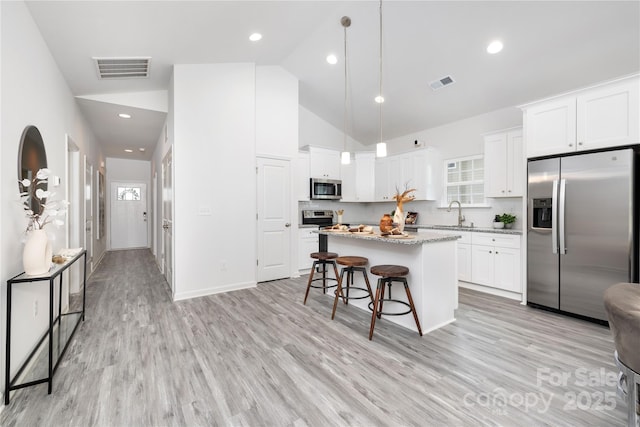 kitchen with visible vents, white cabinets, a kitchen island, decorative light fixtures, and stainless steel appliances