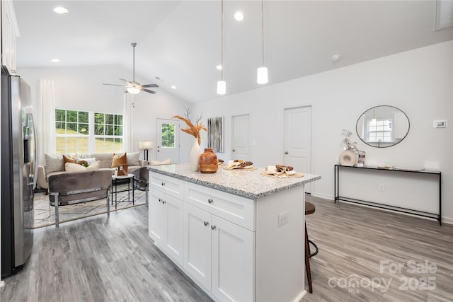 kitchen with stainless steel fridge, a kitchen island, white cabinets, and open floor plan