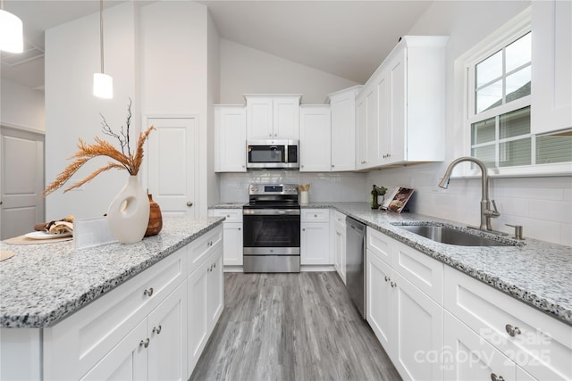 kitchen with a sink, white cabinets, vaulted ceiling, appliances with stainless steel finishes, and decorative light fixtures