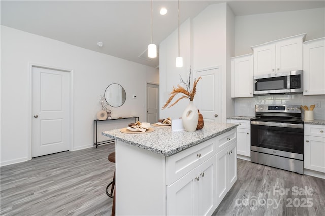 kitchen featuring appliances with stainless steel finishes, a breakfast bar, light stone counters, white cabinetry, and pendant lighting