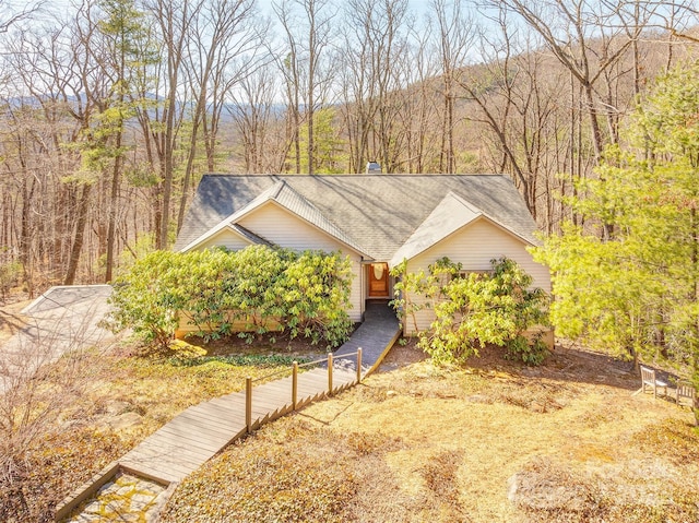 ranch-style house with a shingled roof and a wooded view