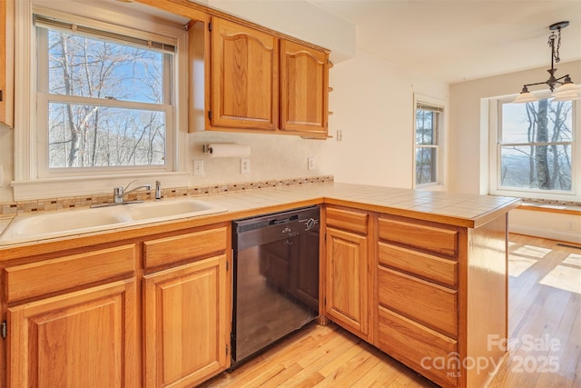 kitchen with a peninsula, a sink, black dishwasher, light wood finished floors, and pendant lighting