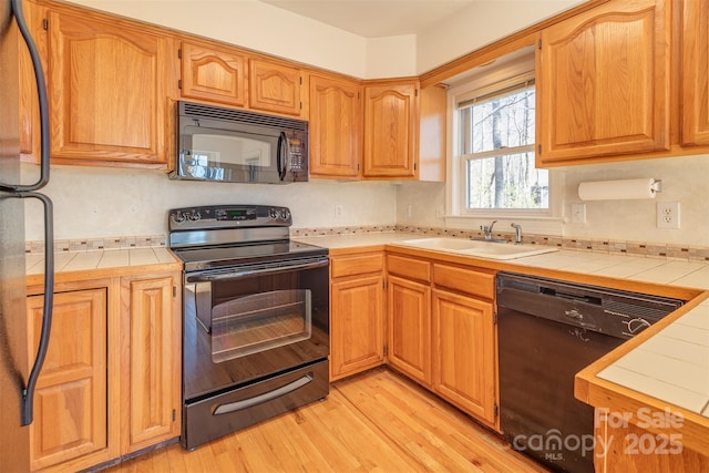 kitchen featuring black appliances, light wood-style flooring, a sink, and tile counters