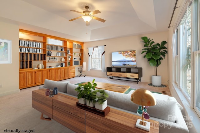 living room with baseboards, ceiling fan, a raised ceiling, and light colored carpet