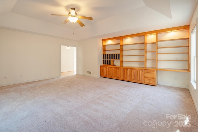 unfurnished room featuring light carpet, a tray ceiling, built in study area, and baseboards