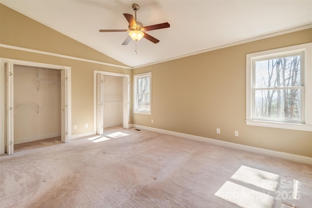 unfurnished bedroom featuring lofted ceiling, multiple windows, two closets, and light carpet