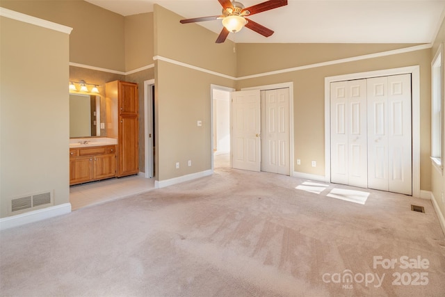 unfurnished bedroom featuring multiple closets, light colored carpet, visible vents, and ensuite bath