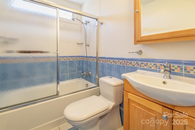 full bath featuring toilet, a wainscoted wall, vanity, tile walls, and combined bath / shower with glass door