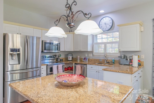 kitchen with white cabinets, a kitchen island, appliances with stainless steel finishes, light stone countertops, and a sink