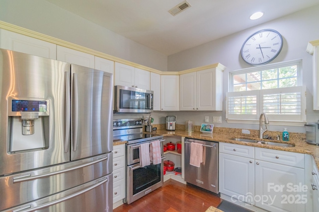 kitchen with light stone counters, a sink, visible vents, appliances with stainless steel finishes, and dark wood-style floors