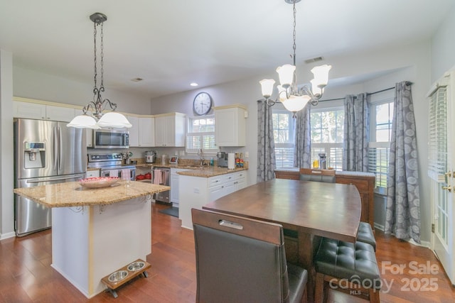 kitchen with dark wood finished floors, stainless steel appliances, visible vents, a kitchen island, and a sink