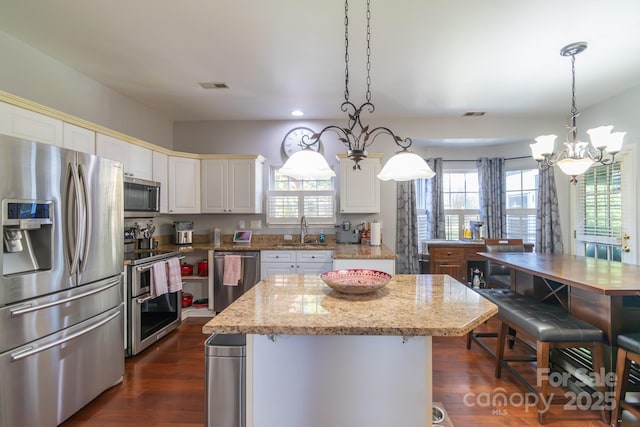 kitchen featuring visible vents, appliances with stainless steel finishes, light stone countertops, a chandelier, and a sink