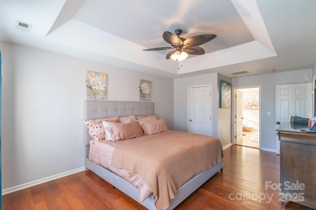 bedroom featuring baseboards, visible vents, a tray ceiling, and wood finished floors