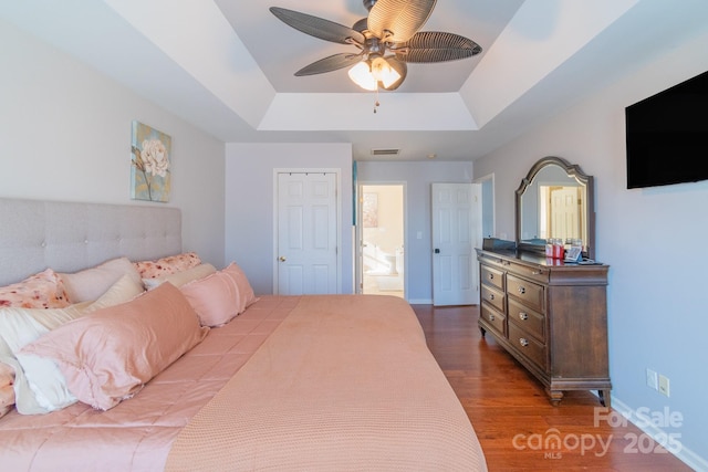 bedroom featuring wood finished floors, a ceiling fan, visible vents, baseboards, and a tray ceiling