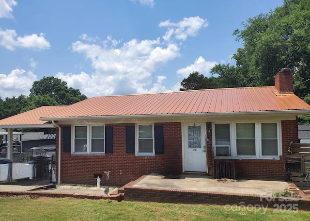 view of front of house with metal roof, brick siding, a chimney, and a patio