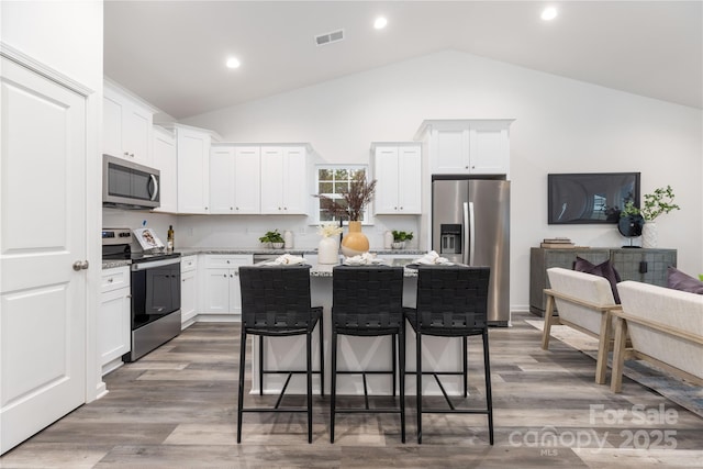 kitchen featuring stainless steel appliances, white cabinets, a kitchen island, light stone countertops, and a kitchen bar