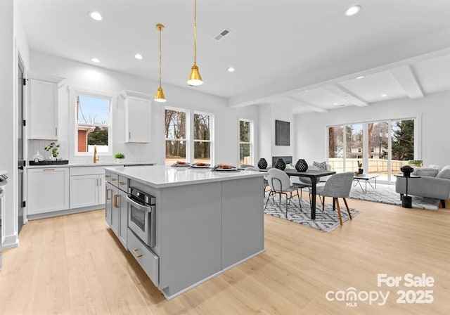 kitchen featuring open floor plan, oven, decorative light fixtures, a center island, and light countertops