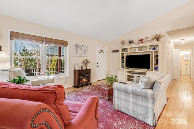 living area with lofted ceiling, light wood-type flooring, baseboards, and a glass covered fireplace