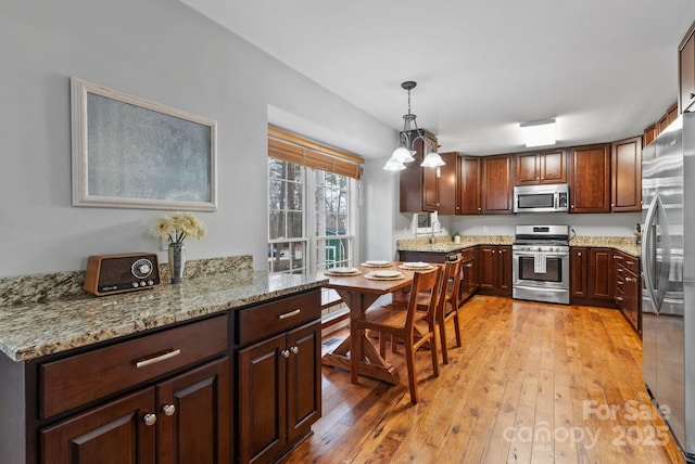 kitchen with stainless steel appliances, light wood finished floors, decorative light fixtures, and light stone countertops