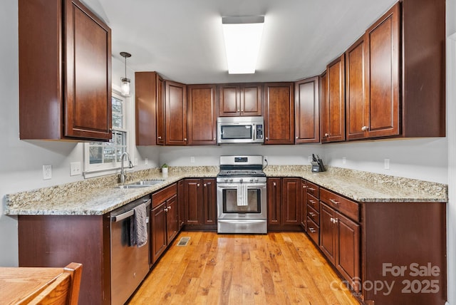 kitchen featuring light wood finished floors, decorative light fixtures, light stone countertops, stainless steel appliances, and a sink